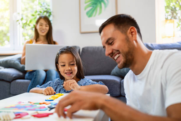 istock Mother working on laptop from home, while her husband and daughter playing with puzzle 1663331259