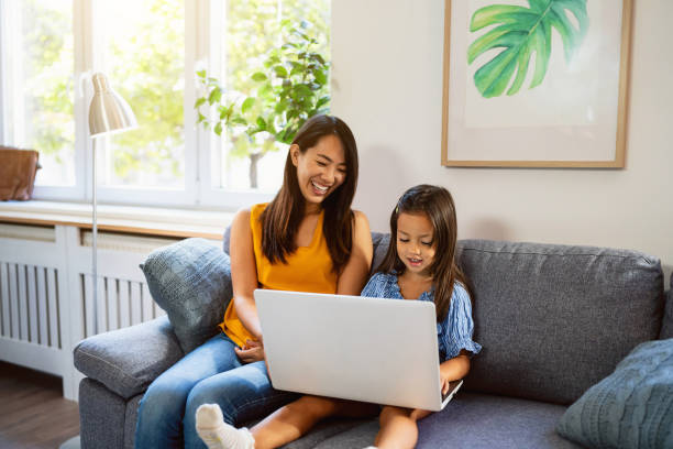 istock Daughter playing on laptop, while her mother sitting next to her on sofa 1663332907