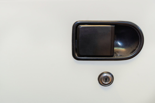 Close-up of an old car's door handle and lock. White car. Black handle.