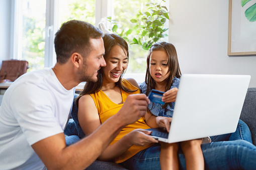 At their home, a multiracial family, a Caucasian father, a Japanese mother and a multiracial daughter together using the laptop for online shopping