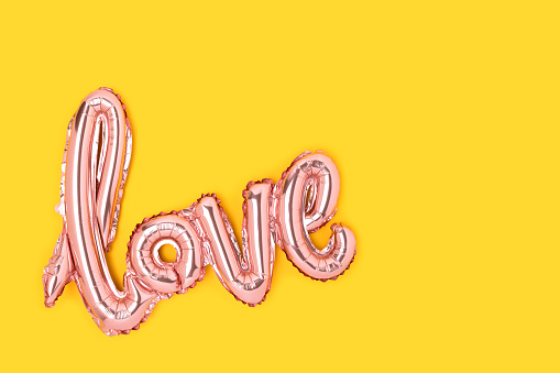 Word Love. Pink foil inflatable balloon on a yellow background.