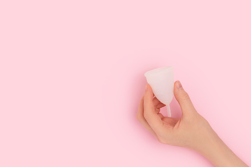 La mano femenina sostiene la copa menstrual blanca sobre un fondo rosa. photo