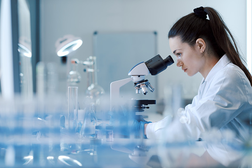 Young female researcher working in the lab, she is examining the samples under a microscope
