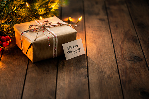 Christmas present wrapped with Kraft paper shot on rustic wooden table. A greeting card with the text 