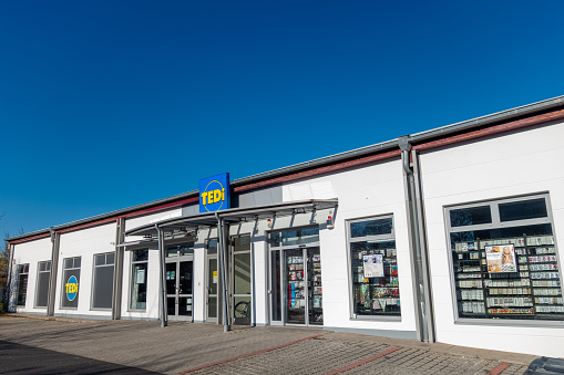 Amberg, Germany - November 13, 2022: Shop of the German non food trading chain TEDI in the town Amberg, Bavaria. Headquarter in Dortmund. More than 2950 shops in 15 countries. Wide assortment with decorating supplies, clothes, housewares, do-it-yourself items, stationery and so on. Sunny sunday afternoon with clear blue sky.