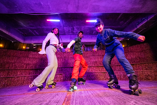 Low angle view of male and female friends in 20s and 30s wearing retro outfits and looking at camera while freestyle skating.