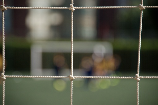 This dynamic image captures the heart-pounding excitement of a football match, with a focus on the intricacies of the game. In the foreground, a close-up of the football net stands tall, its mesh texture and goalpost vividly in focus. Behind it, a blur of players in action creates a sense of energy and anticipation. This image beautifully encapsulates the essence of the sport, where precision and strategy meet the rush of competition on the field