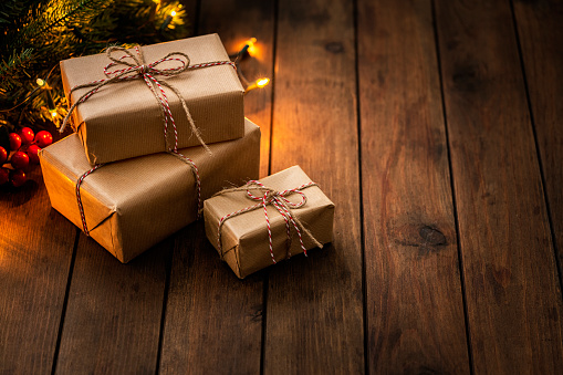 High angle view of three Christmas presents wrapped with craft paper shot on rustic wooden table. Christmas lights and pine branches complete the composition. Copy space available. High resolution 42Mp studio digital capture taken with Sony A7rII and Sony FE 90mm f2.8 macro G OSS lens