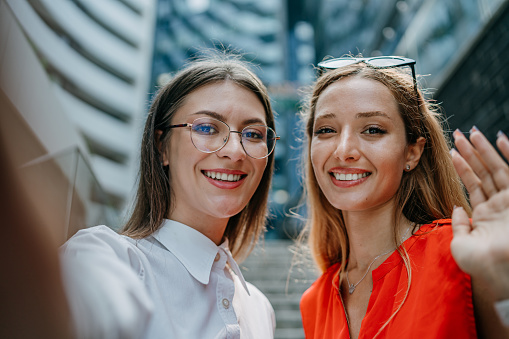 In the heart of the business hub, two dynamic women pause from their busy schedules to share a moment with the camera, symbolizing their partnership and shared journey