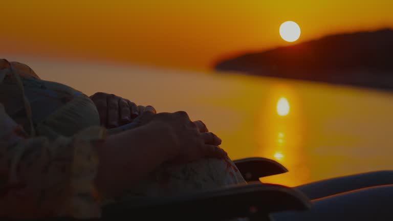 Pregnant woman touching her bump and relaxing on chair by sea