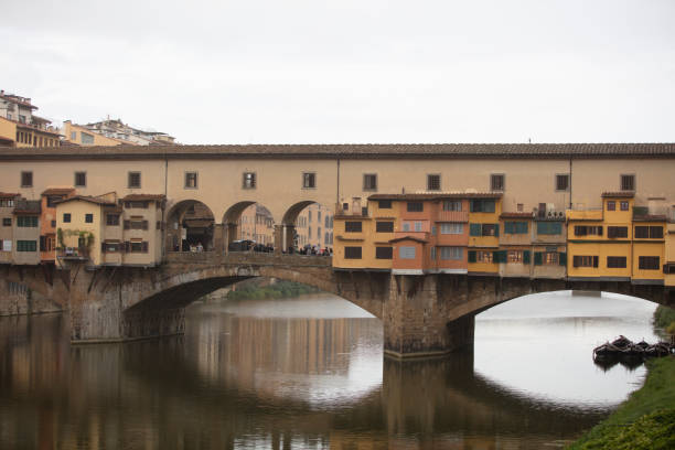 Florence, Italy - 8 Aug, 2023: A serene view of the historic Ponte Vecchio bridge and the Arno River with a small boat rowing pass in Florence, Italy. Vibrant reflections on the water create a picturesque scene.