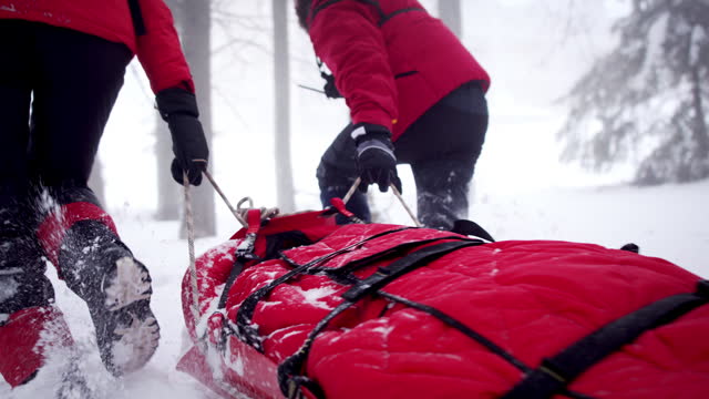 Mountain rescue service provide operation outdoors in winter in forest, pulling injured person in stretcher.