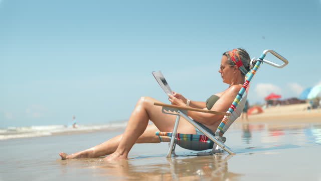 Mature woman sitting on beach chair at water's edge
