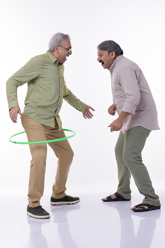 Full length portrait of two cheerful elderly men with hula hoops isolated on white background