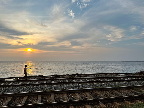 Colombo, Sri Lanka - January 18, 2023: Stock photo showing close-up view of metal railway the line and gravel of southern line diesel railroad track in Colombo, Sri Lanka running parallel to the coast with waves breaking on the rocky shore.