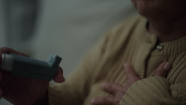 Senior woman using asthma inhaler at home.