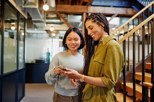 Colleagues standing and smiling cheerfully at video on cellphone in modern office