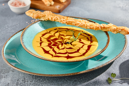 A closeup horizontal view of a bowl of creamy pumpkin soup with crostini. The texture of the soup and the gray concrete background create a feast for the eyes.