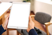 Close up  woman's hands are actively engaged with a tablet featuring a blank screen mock-up, showcasing the modern world of technology at work.