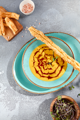 A vertical, top view of pumpkin soup with crostini, providing ample copy space. Set against a gray concrete background, the composition is minimalist yet inviting.