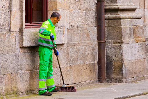 Street sweeper, garbage collector in the street,  broom. Street sidewalk. Stone building exterior. Copy space available. Santiago de Compostela, Spain.