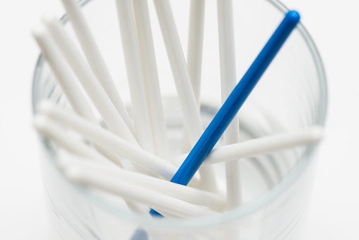 One blue stick among a lot of white sticks in a drinking glass on white background. Representing individuality and being different.