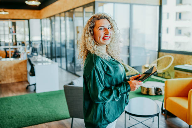 istock Side view of businesswoman holding digital tablet, smiling at camera in breakout space 1663605499