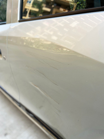 Stock photo showing close-up view of a white car rear passenger door  that has been freshly gouged and scratched after a parking accident. This photo concept shows primer and colour coat scratches in need of respraying at a garage, and maybe a car insurance claim.