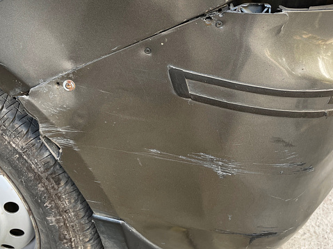 Stock photo showing close-up view of a silver car rear bumper wheel arch that has been freshly scratched and dented after a parking accident. This photo concept shows primer and colour coat scratches in need of respraying at a garage, and maybe a car insurance claim.