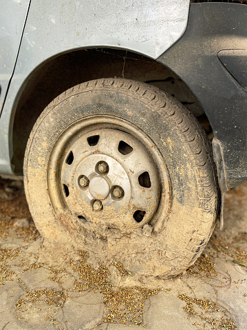 Stock photo showing close-up view of a silver-blue car with a flat tyre and covered in mud. This photo concept shows a car in need of a car detailing.