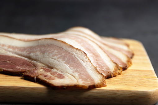 Guanciale dried speck а ham. Italian cured meat product prepared from pork jowl or cheeks sliced on wooden board.