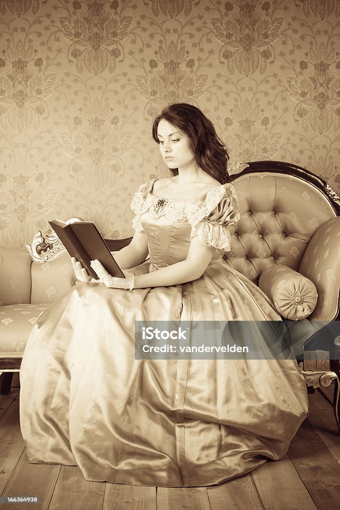 Victorian-style Girl Reading Sepia image of a young adult in a Victorian-style dress sitting on a chaise longue reading a book - possibly a bible or other worthy tome. 18-19 Years Stock Photo