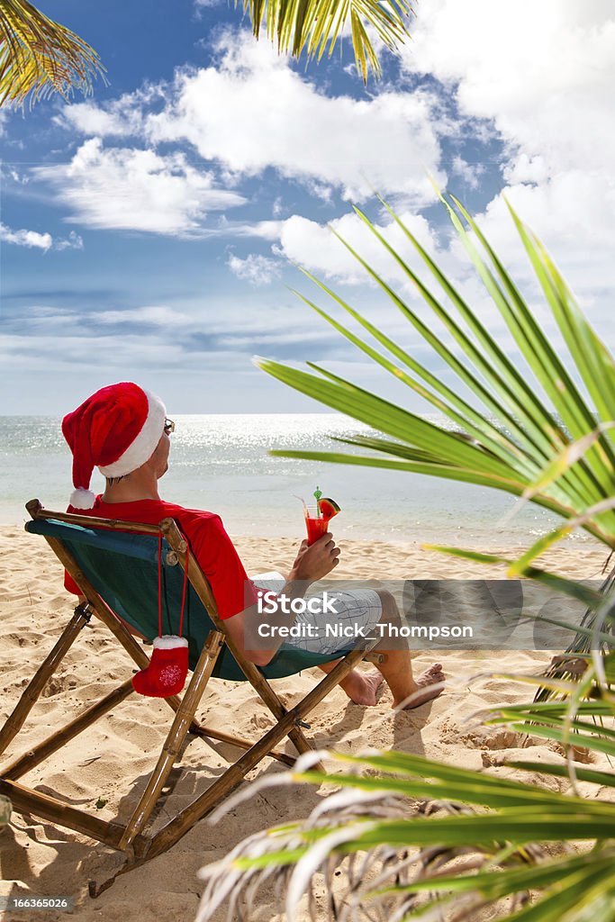 Uomo in Cappello di Babbo Natale con cocktail seduto sulla spiaggia - Foto stock royalty-free di Adulto