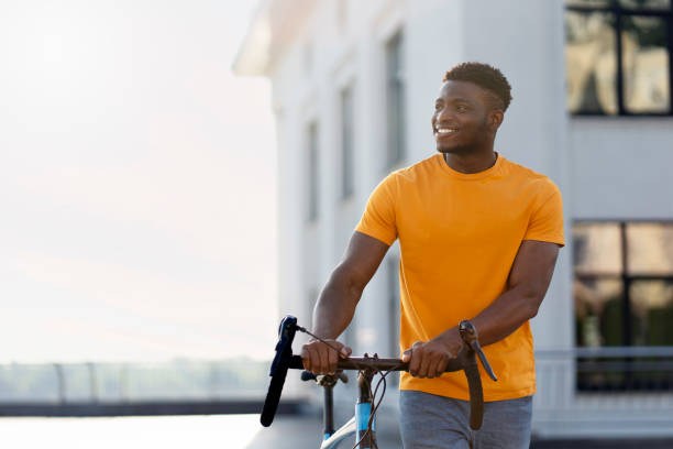 Handsome smiling african american man looking away while standing on urban street near bicycle