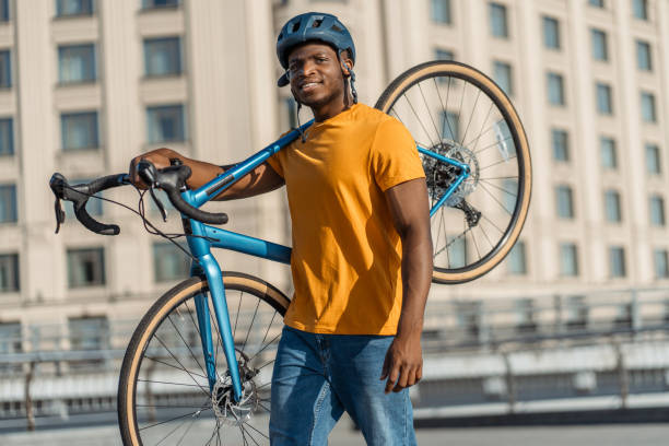 Portrait of smiling positive Nigerian man holding bicycle wearing safety helmet
