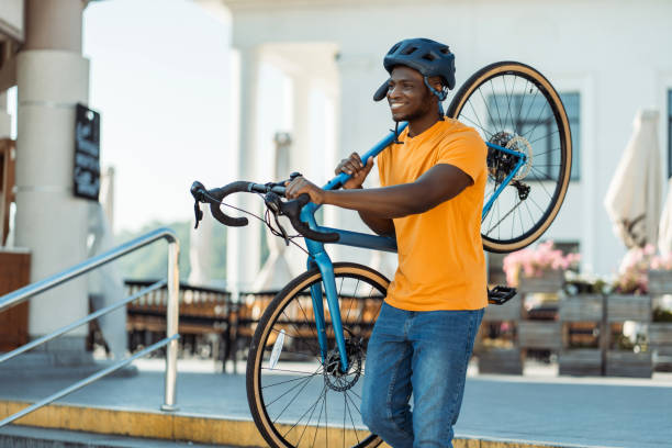 Portrait of smiling positive Nigerian man holding bicycle wearing safety helmet