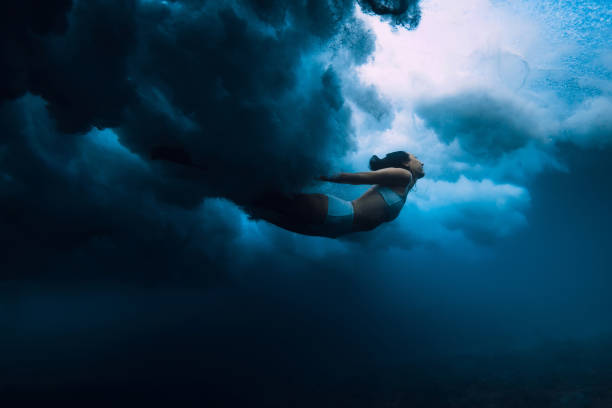 istock Woman dive under ocean wave. Duck dive under crashing barrel wave in transparent ocean 1663672402