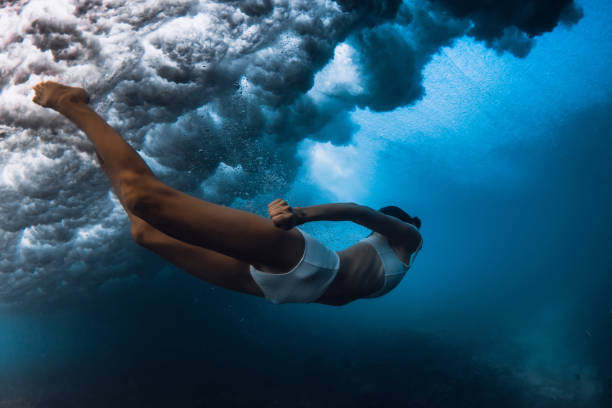 istock Woman dive under ocean wave. Duck dive under crashing barrel wave in transparent ocean 1663673577