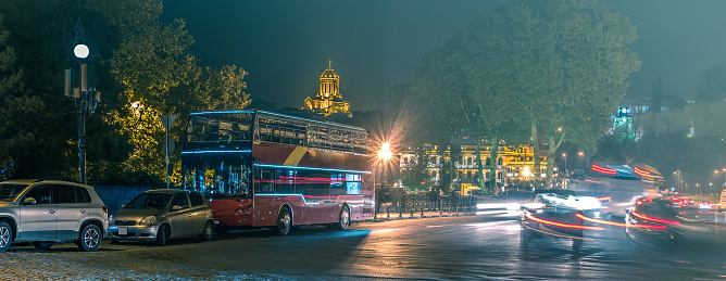 red sightseeing bus on Tbilisi night road with cars
