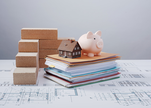 Bricks, piggy bank and pile of paperwork: home building process, investment and construction concept