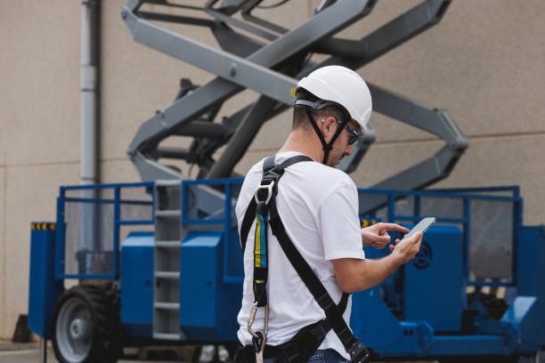 istock Engineer in a hard hat and harness writing on a smartphone near an aerial work platform (AWP). 1663687430