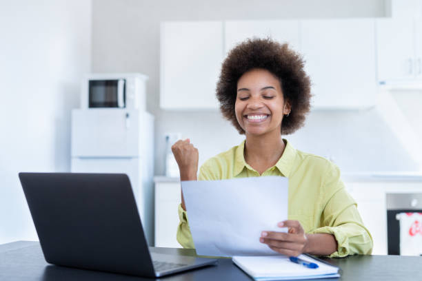istock Happy smiling remote working young black female receive postal letter from company office about project report approval. Glad millennial afro american employee reading good news from paper document 1663705726