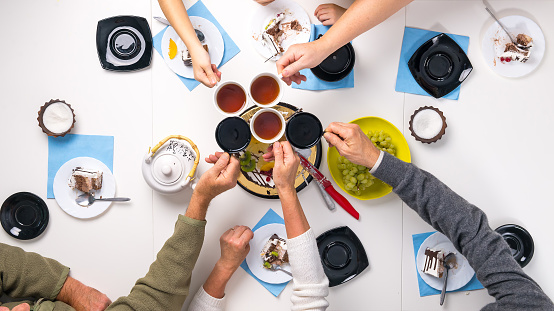 people clanging cups with tea together at the table with delicious desserts, top view