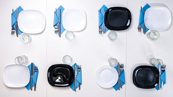 table setting for eight persons with white and black plates, glasses and napkins, top view