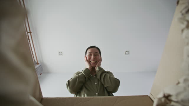 Excited Asian woman opening cardboard box at home