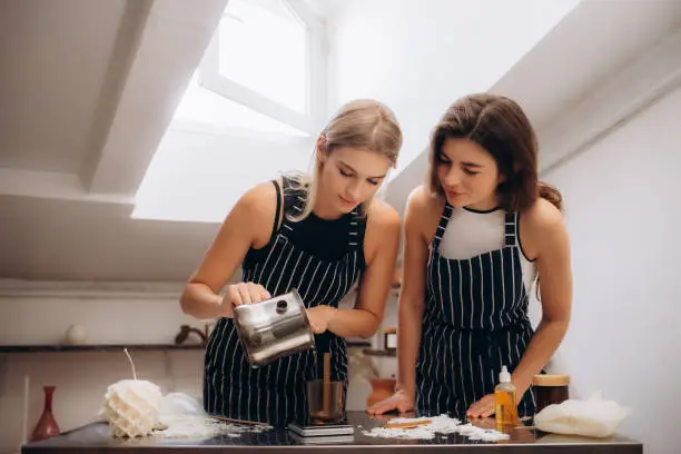 Two women pour wax into a mold for a candle.