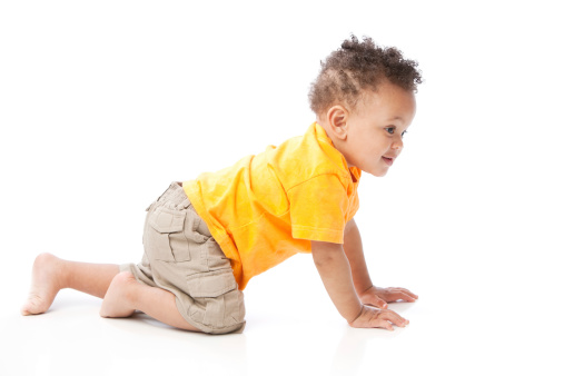 A full length image of a black toddler little boy wearing a bright orange shirt. It is a side view of him crawling.