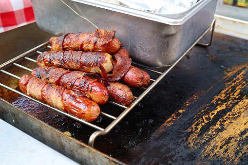 Five Plump Bratwurst or Hot Dogs on an old fashioned charcoal barbecue Grill with Flames surrounding them.