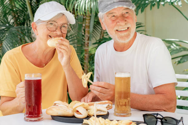 istock Attractive cheerful senior couple sitting at pub restaurant table eating sandwiches on a sunny summer day while enjoying glasses of cold beer 1663759477
