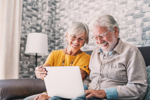 istock Pretty elderly 70s grey-haired couple resting on couch in living room hold on lap laptop watching movie smiling enjoy free time, older generation and modern wireless technology advanced users concept 1663759487